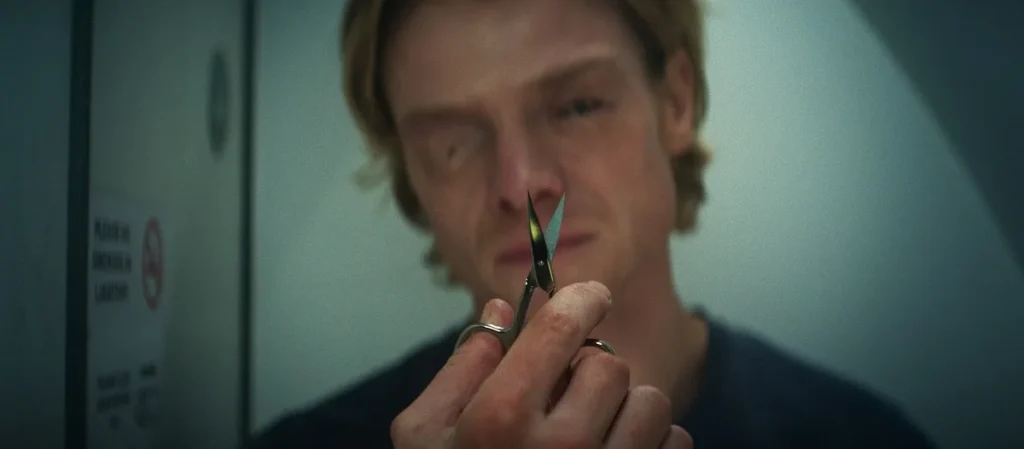 Tom Rhys Harries as Matt Hagen pulling at his changing face with tweezers in a Clayface body horror scene